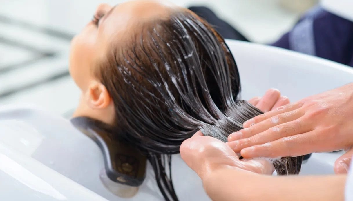 Una persona si gode un Trattamento Capelli nel salone di bellezza, dove mani esperte applicano lo shampoo e massaggiano delicatamente il cuoio capelluto prima di procedere con una piega impeccabile.
